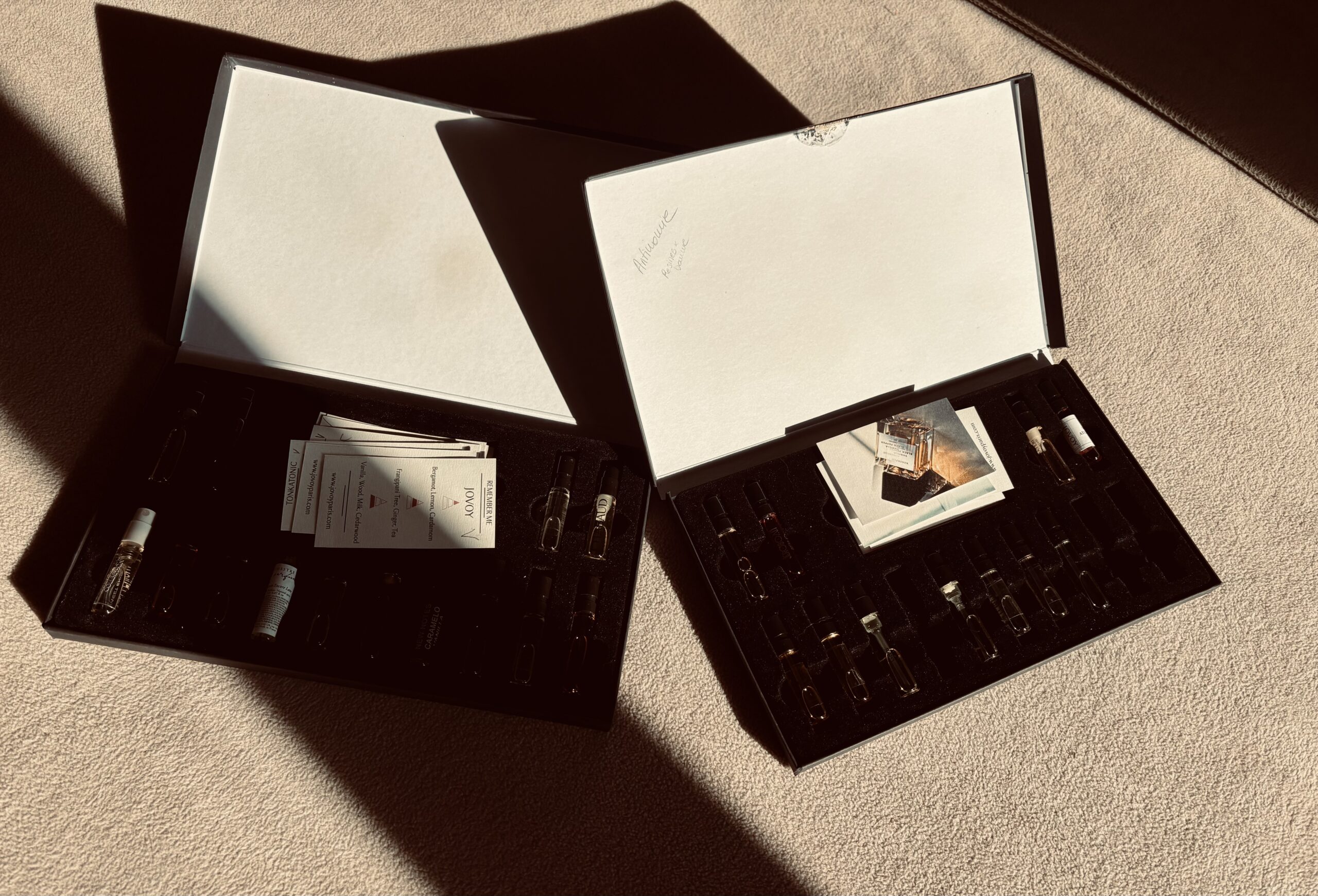 Deux coffrets ouverts contenant des échantillons de parfums et leurs cartes, dans la lumière du soleil.